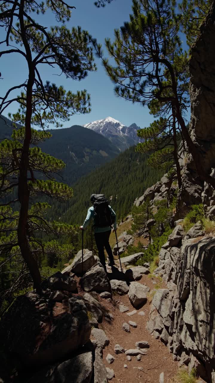 Un excursionista recorre un sendero montañoso rocoso, capturado desde un ángulo trasero.