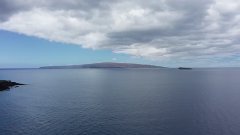 Toma-Aérea-Baja-Volando-Sobre-El-Océano-Hacia-El-Cráter-Molokini-Y-La-Isla-Sagrada-Hawaiana-De-Kaho&#39;olawe-Frente-A-La-Costa-De-Maui-En-Hawai&#39;i