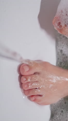 woman feet in warm foamy bathtub water closeup. lady enjoys body care procedures washing legs in cozy bathroom closeup. pleasure of hygienic routine