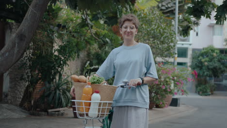 cheerful girl posing with bike and basket of groceries outdoor