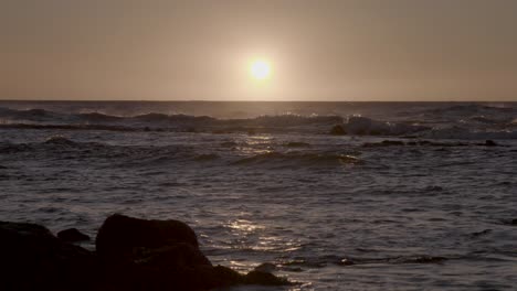 tiro de la playa de hawaii mirando las olas chocando contra las rocas en el océano mientras el sol cae por debajo del horizonte