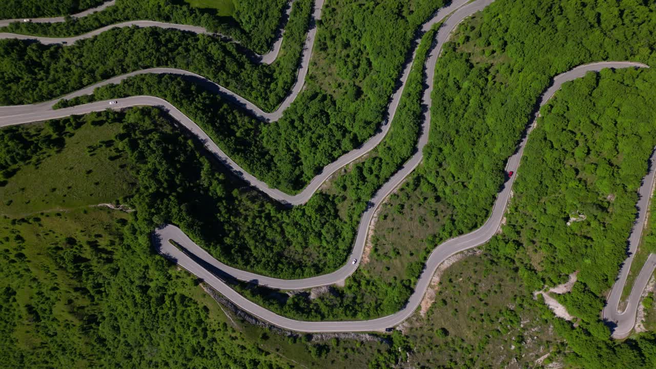 Crisp aerial shot of switchback curves slicing across mountain slopes surrounded by vibrant greenery. Shot at Selvino, Italy (Selvino, Italia)