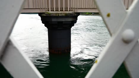 sea water splashing beneath submerged concrete bridge foundation view through railings dolly left