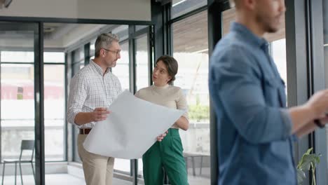 diverse male and female architects discussing over a plan at office