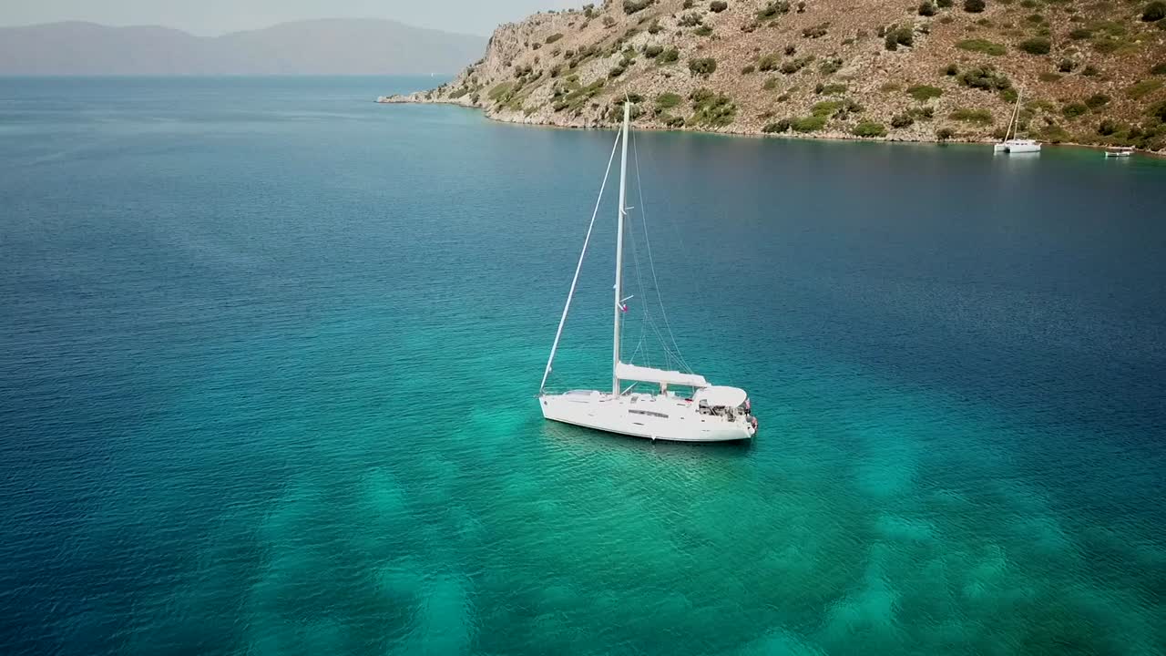 Drone flying backward from sailing boat on a quit anchorage bay with turquoise waters in Turkey.