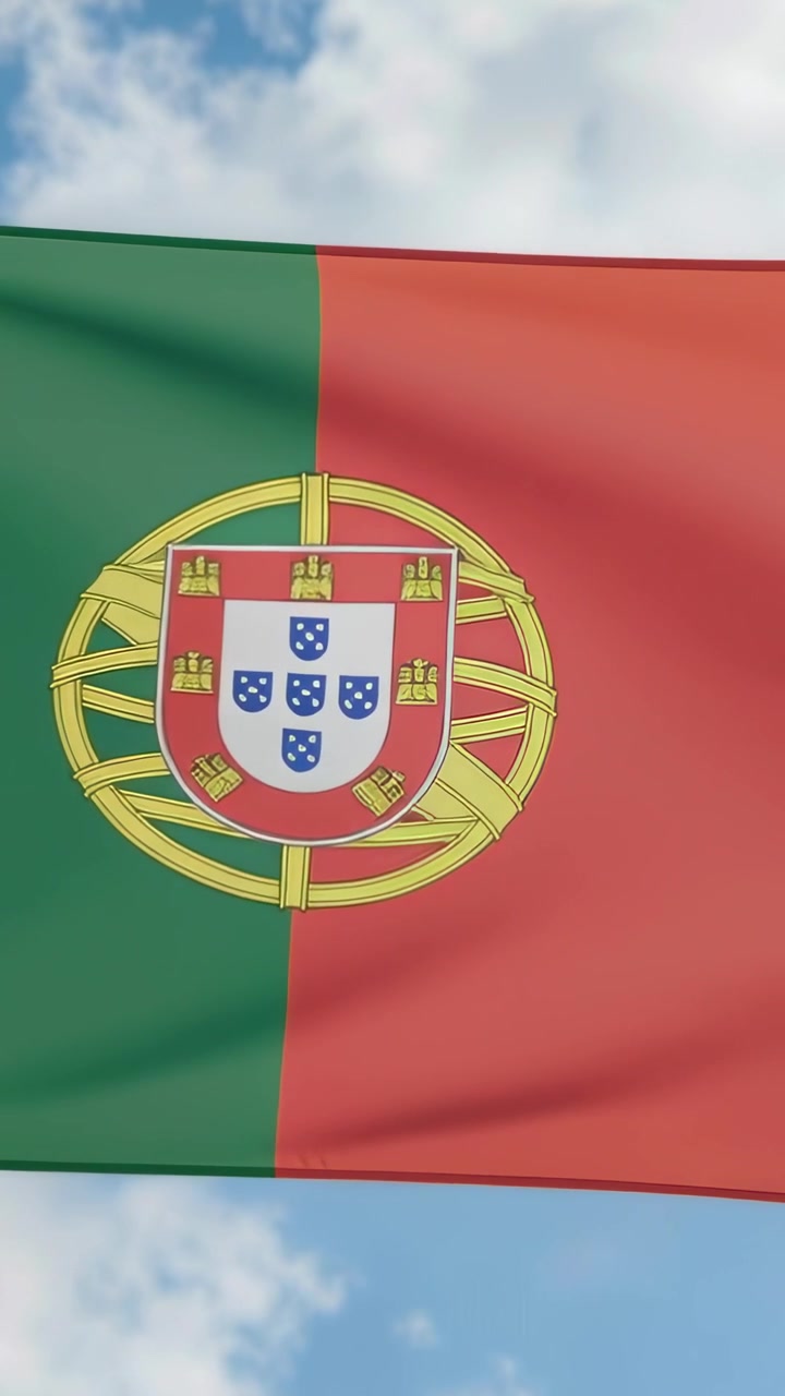 Vídeo vertical: Bandeira portuguesa tremulando contra o céu azul devido a rajadas de vento, revelando o brasão de armas