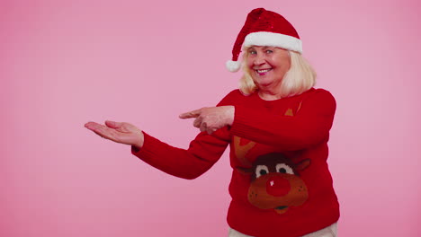 Grandmother-in-Santa-Christmas-sweater-showing-thumbs-up-and-pointing-empty-place,-advertising-area