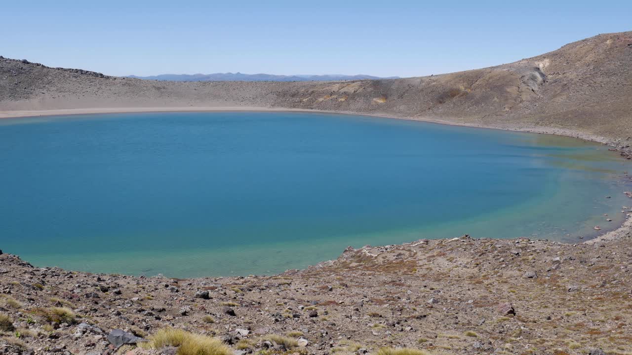 panorámica a través de un lago volcánico azul yermo hasta una mujer rubia tomando una foto telefónica