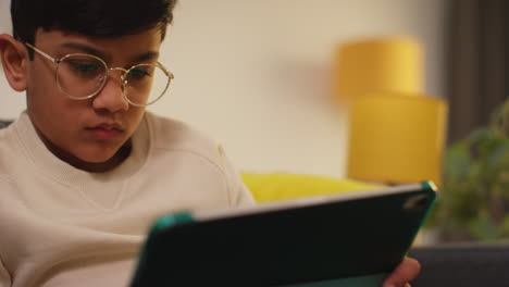 close up of young boy sitting on sofa at home playing games or streaming onto digital tablet 5