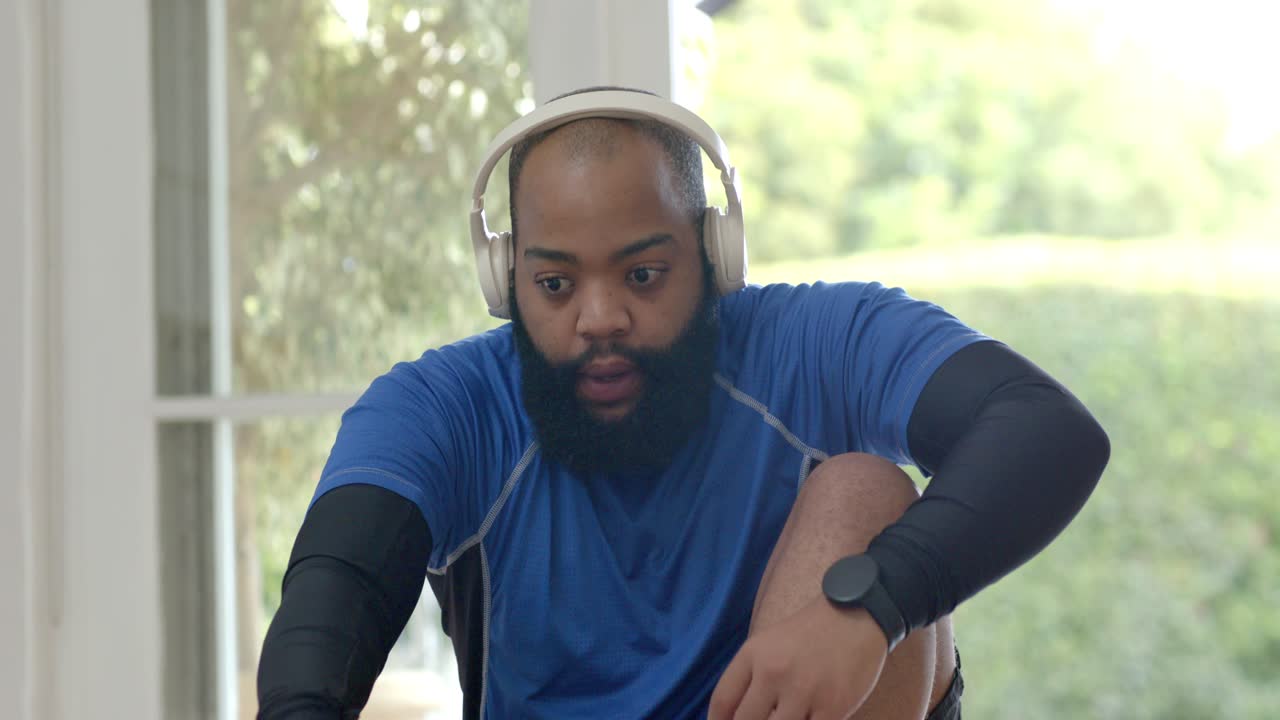 Man starting by drawing knee up, wearing headphones, monitoring wristwatch, boosting core fitness