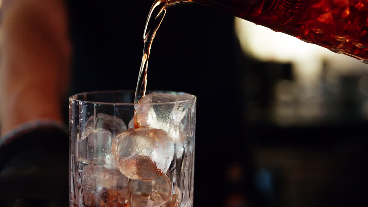 Barman straining alcohol in a glass with ice cubes