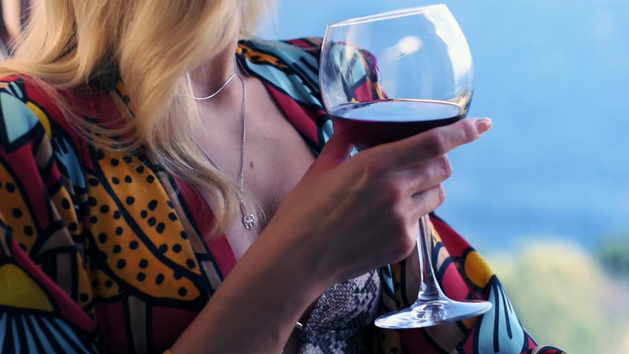 Woman holding red wine glass in hand looking through the window