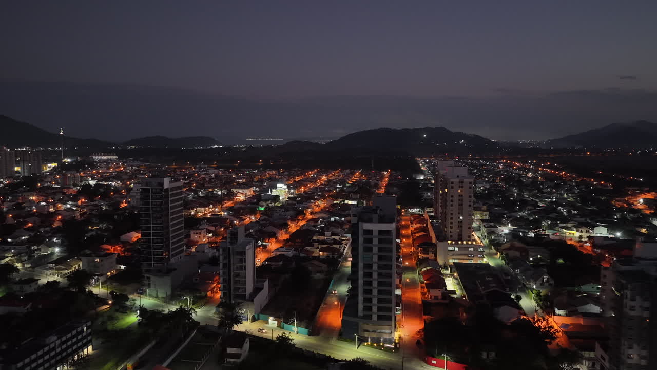 Panoramic aerial fly over the illuminated city streets of Penha municipality with glowing buildings at night, Santa Catarina, Brazil