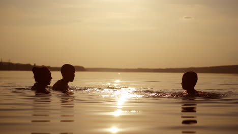 woman and two children playing in water in the evening. silhouette of female and boys having fun in the river at sunset. mother throws up her son into the water.