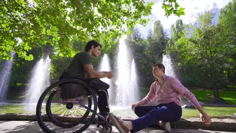 joven discapacitado sentado en una silla de ruedas hablando con su amigo al aire libre.