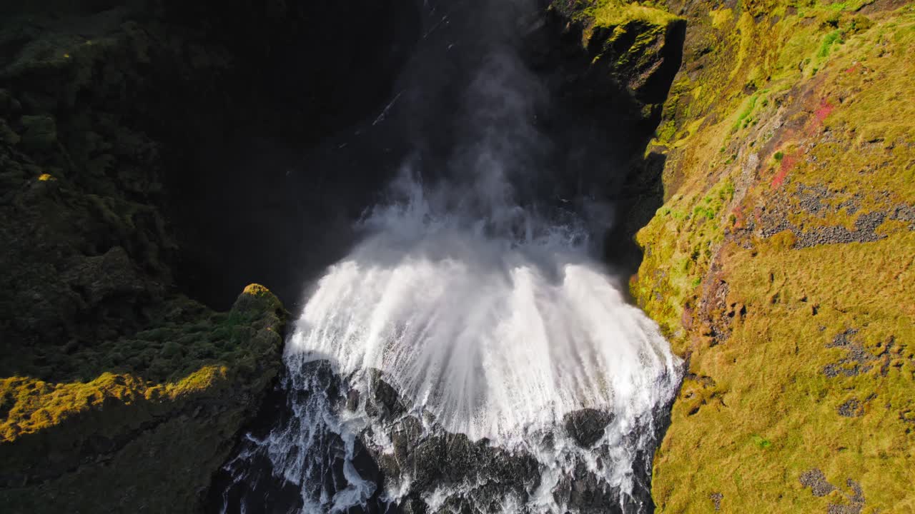 drone aéreo de arriba hacia abajo volando sobre una gran cascada islandesa brumosa al atardecer cálido