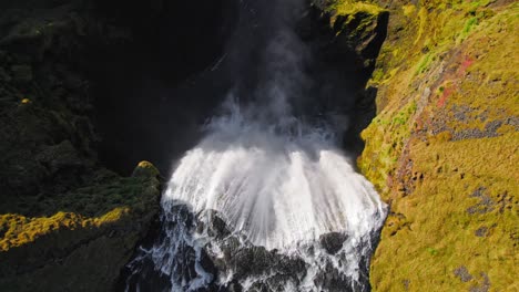 top-down aerial drone flying over large misty icelandic waterfall at warm sunset