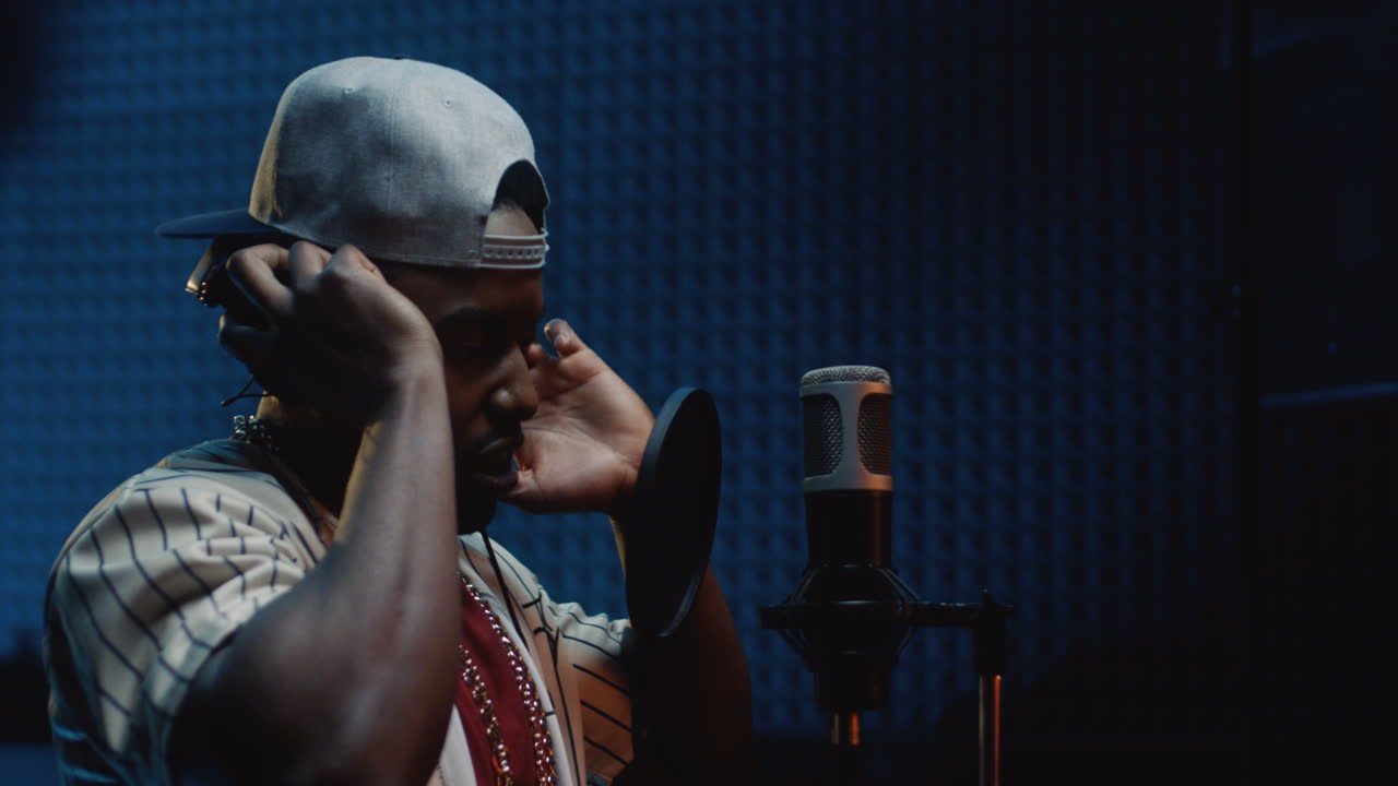 joven cantante elegante y guapo cantando blues o r'n'b en el micrófono durante la grabación en el estudio de sonido