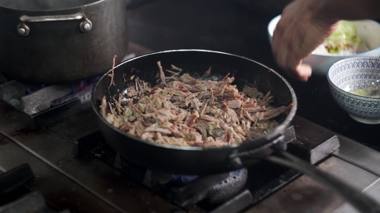 View of a chef hands adding vegetables to a beef stew in a pan in a restaurant kitchen