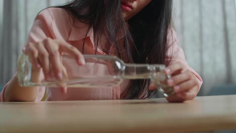 close up of drunk asian woman pouring vodka in a shot glass and cheer to camera before drinking at home