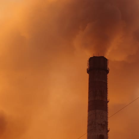 Thick fumes from industrial chimneys smoking. Clouds of dirty emissions pollute the atmosphere. Puffs of smoke on the evening sky. Polluting factory at sunset