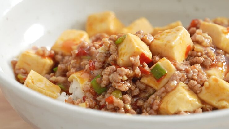Pouring stir-fried mapo tofu with hot spicy sauce over white rice in a bowl at home