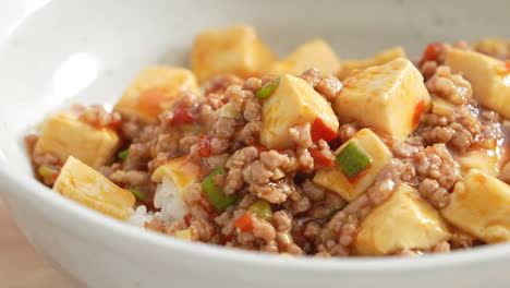 pouring stir-fried mapo tofu with hot spicy sauce over white rice in a bowl at home