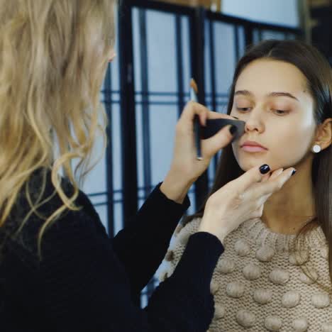 makeup artist does a young woman's make up in studio