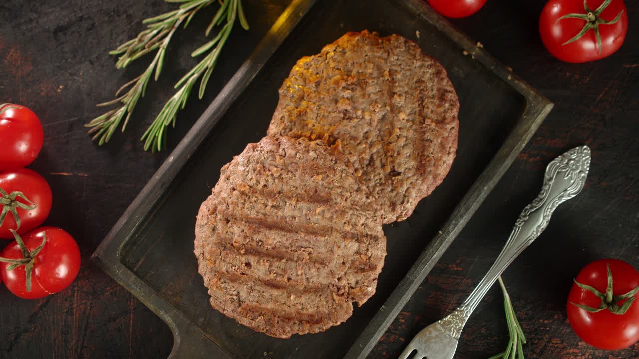Fried burger meat on a cutting board with tomatoes rotates.