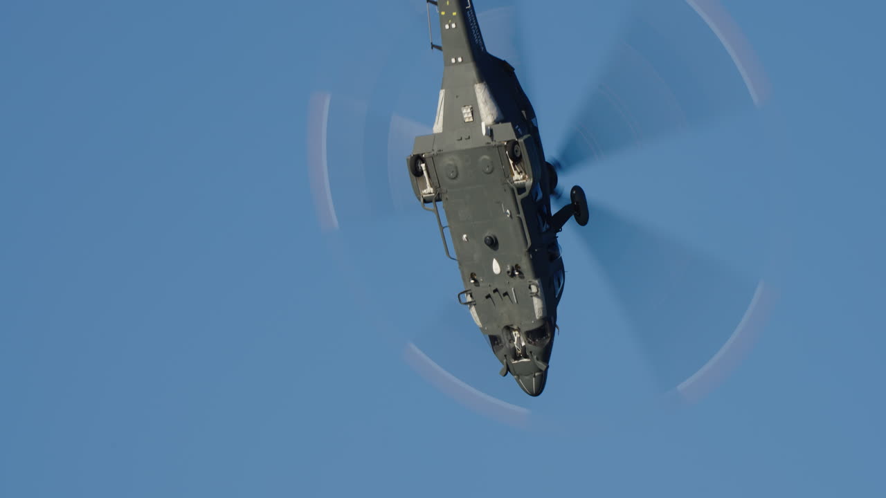 Dark Military Helicopter Flying and Maneuvering in Clear Blue Sky