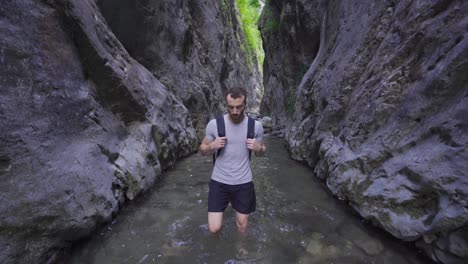Barefoot-man-walking-in-creek-between-cliffs.