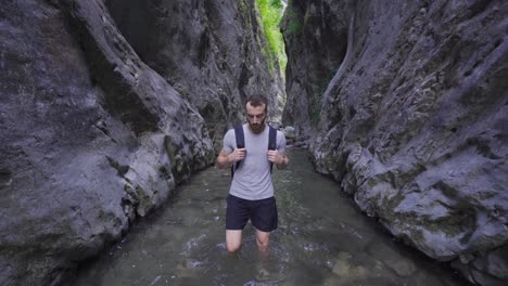 barefoot man walking in creek between cliffs.