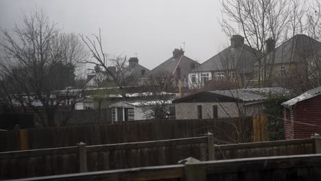 light snow falling in back gardens with garages in harrow on overcast day