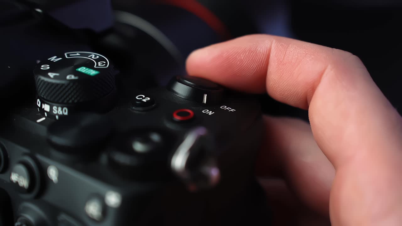 Primo piano di una mano che accende l'interruttore di alimentazione su una fotocamera mirrorless, con ghiera delle modalità e un morbido bokeh da studio — ideale per attrezzatura da creator e b-roll tecnologico.