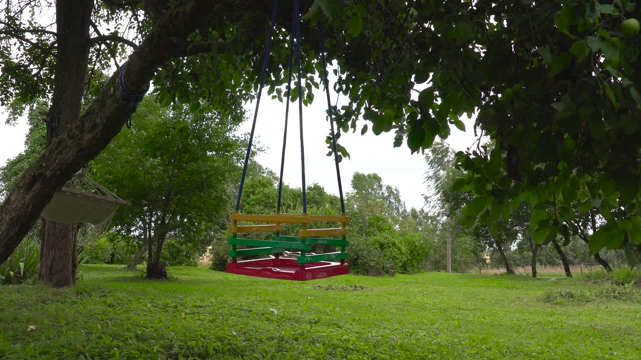 Empty children swing gently move in windy countryside garden, Latvia