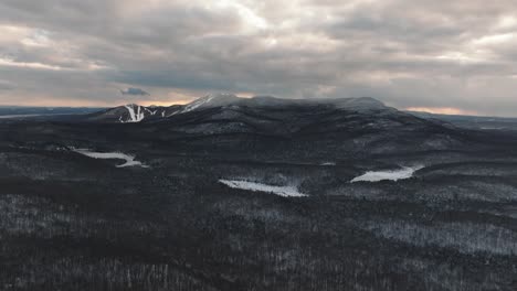 monochrome of a snowy forest and mountains under clouded sky in orford, quebec, canada
