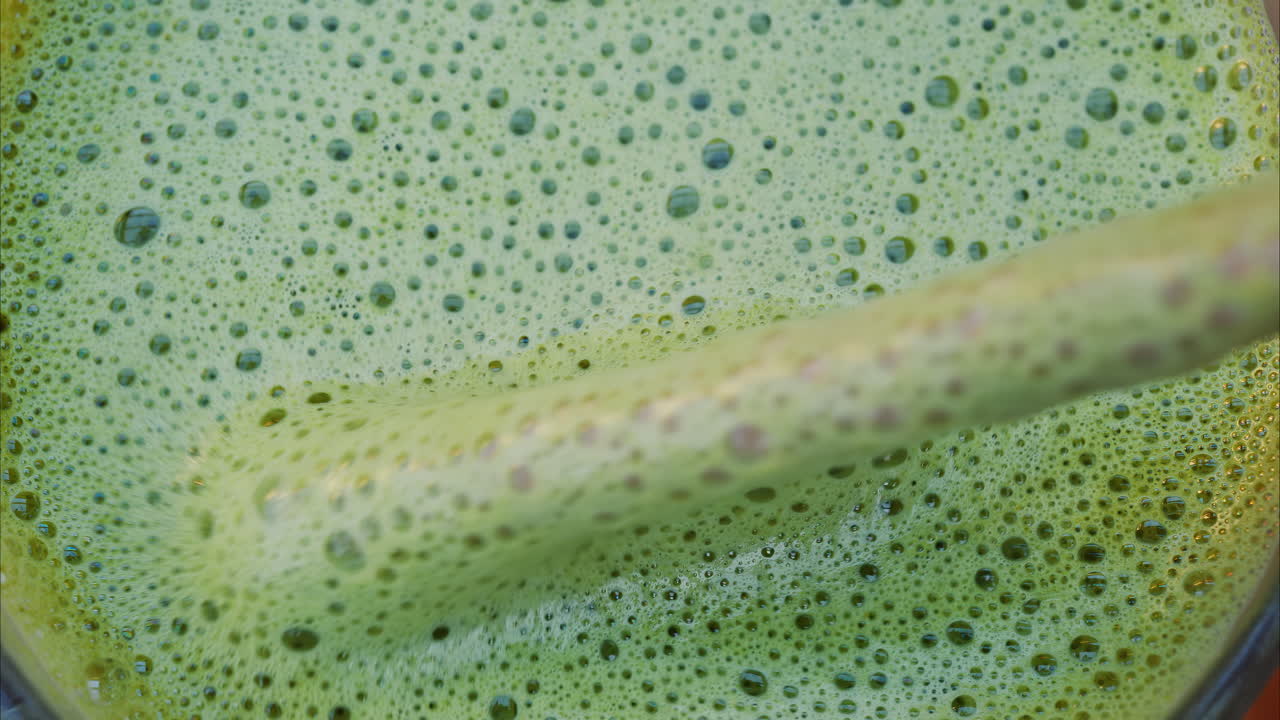 Close up of a woman mixing a matcha latte with a paper straw at a cafe