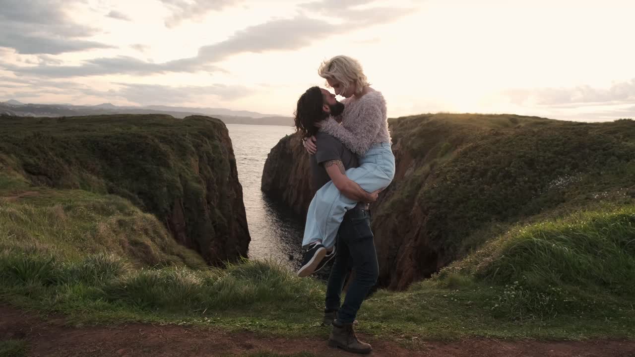 Man lifting woman on cliff near sea