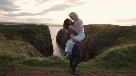 man lifting woman on cliff near sea