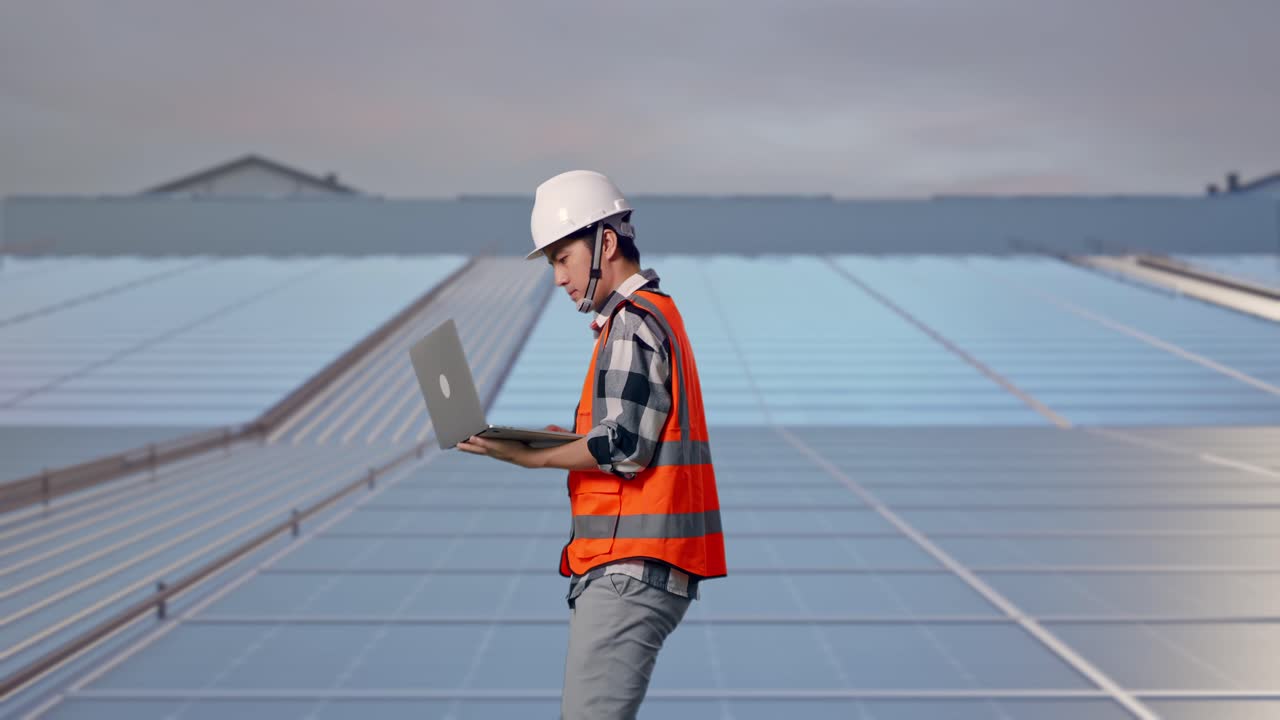 Tampak Samping Insinyur Pria Asia Menggunakan Komputer Sambil Berjalan di Panel Surya Atap Industri