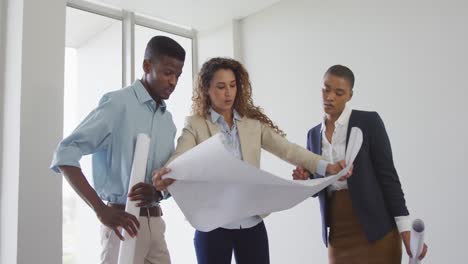 biracial male and female architects checking architects plans in modern office