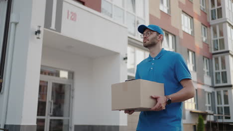 young delivery man wearing glasses and gloves holding box use phone walking on street quarantine outdoor shopping package pandemic postman self isolation slow motion