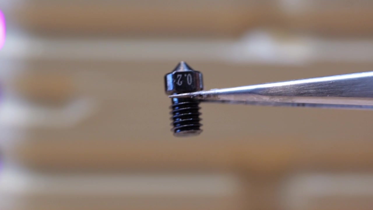 Primo piano estremo di pinzette metalliche che tengono un minuscolo ugello di precisione da 0,2 mm per una stampante 3D