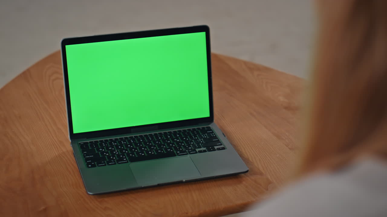 Laptop con schermo verde posizionato sulla scrivania, primo piano. Donna sconosciuta che guarda un mockup.
