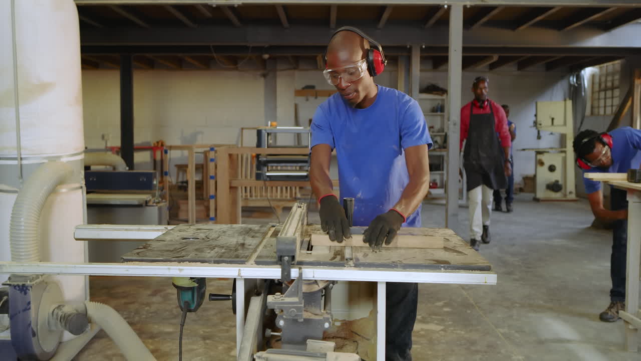 Picking earmuffs, African American man aligning panel in shop using table saw, measuring precisely