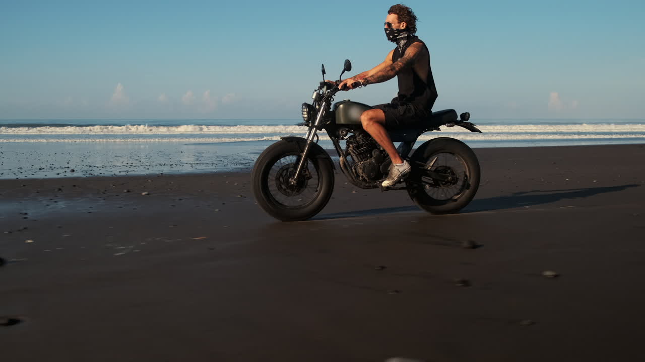 hombre montando una motocicleta en una playa al amanecer o al atardecer