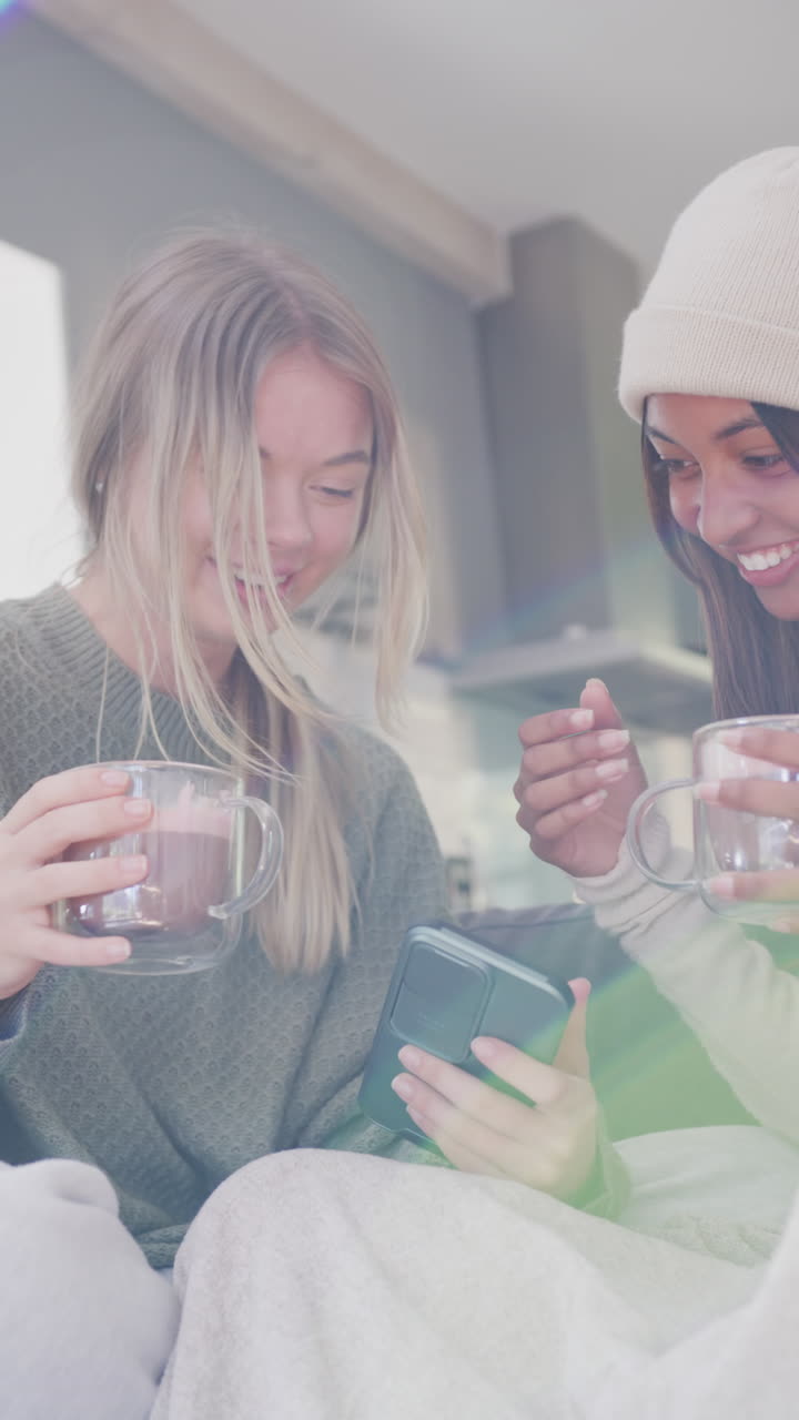 Vertical video of happy diverse teenager girls with smartphone and coffee at home, slow motion