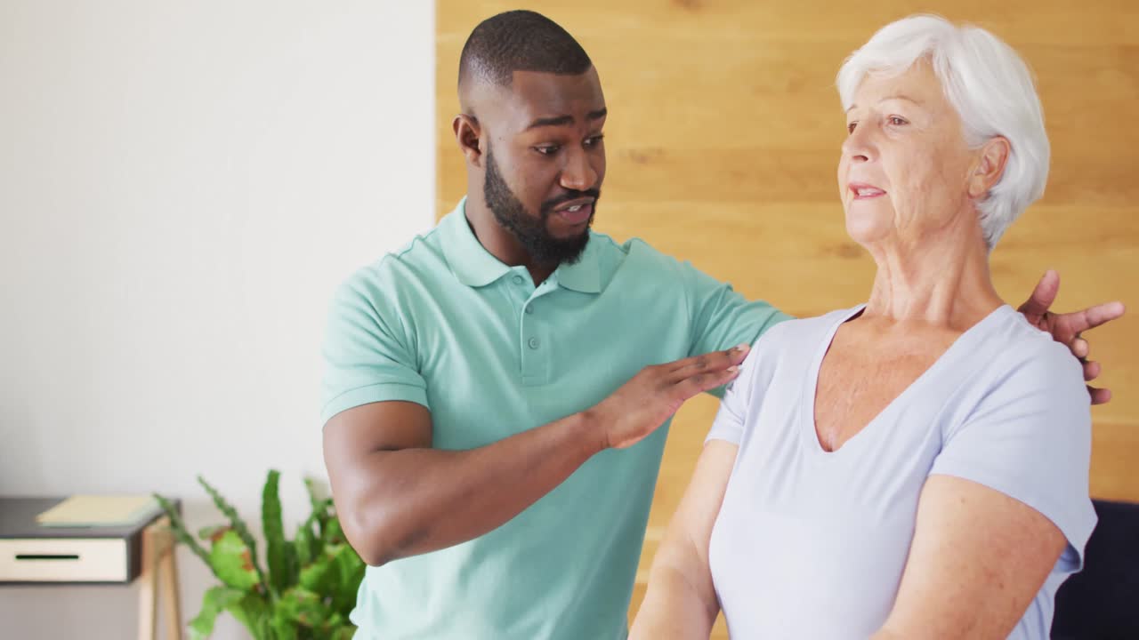 Video of happy african american male physiotherapist exercising with caucasian senior woman