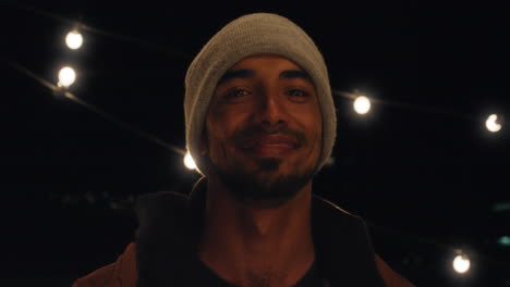 retrato de un joven hispano atractivo en la azotea por la noche sonriendo feliz con apariencia confiada disfrutando de la vida nocturna urbana con luces en el fondo