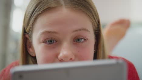 close up of teenage girl wearing orthodontic braces lying on bed at home looking at screen of digital tablet - shot in slow motion